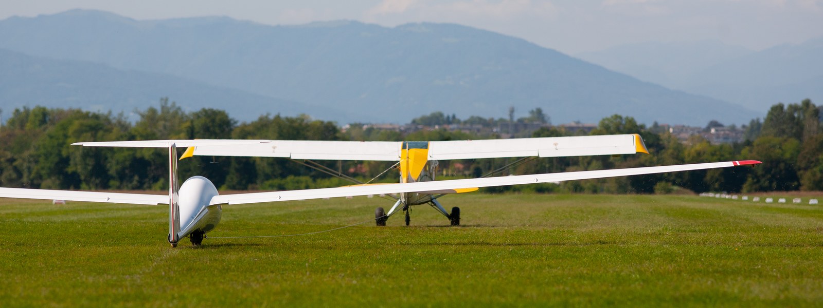 Aliante e aereo da traino agganciati sul prato di Belluno, pronti al decollo, con le montagne dietro